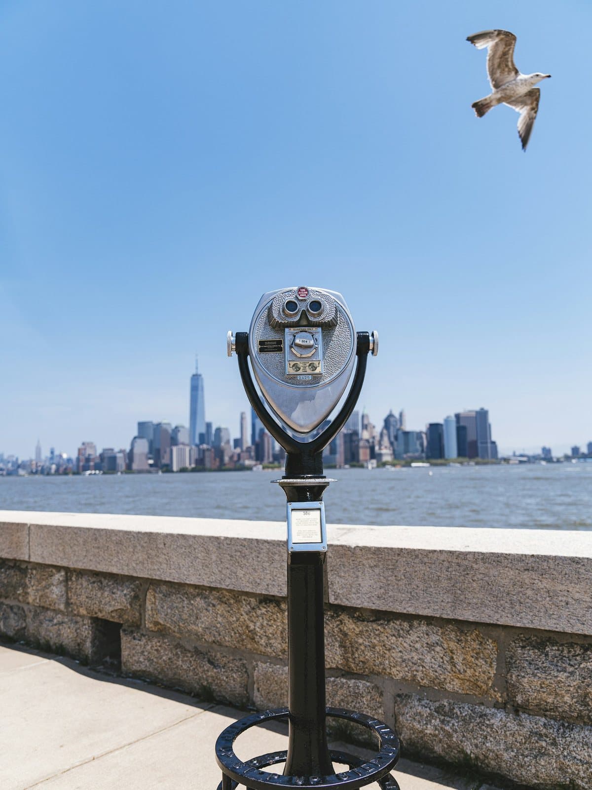 A viewing telescope on the waterfront promenade, skyline beyond